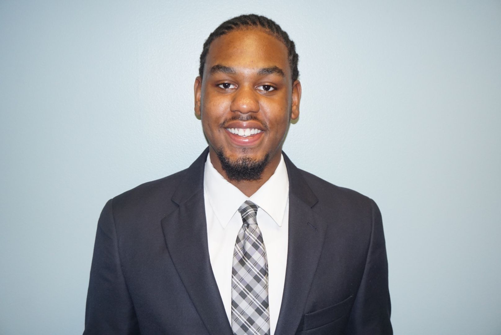 Man in a suit with a checkered tie smiling against a light blue background.